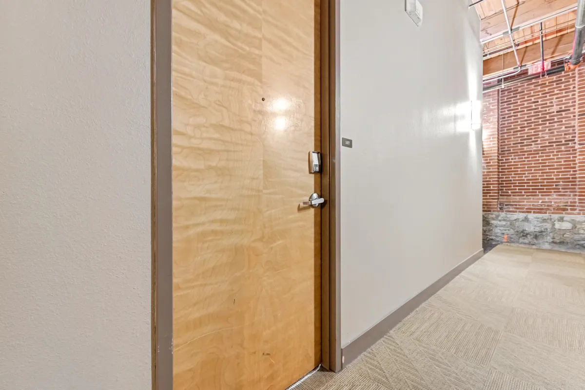 A close view of a wooden door framed by exposed brick and a carpeted floor, conjuring the feeling of arrival. The scene suggests a blend of historic character and a welcoming atmosphere, echoing the building's preserved heritage.