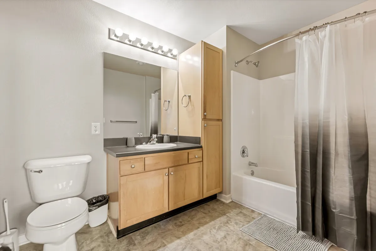 A calming bathroom scene with a vanity and sink, bathtub with shower curtain, and a mirrored cabinet. The space is both functional and soothing, with soft lighting and clean, modern fixtures that complement classic tilework.