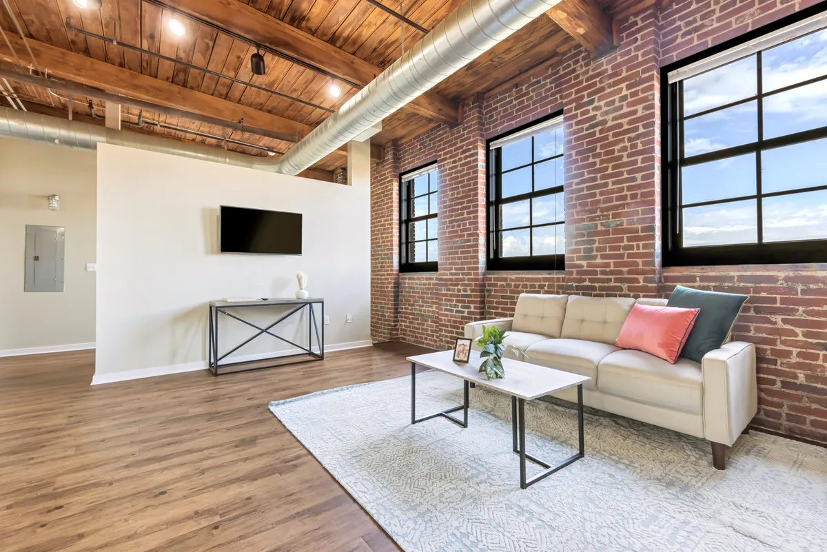 A stylish living area with a modern sofa and coffee table sits in front of large windows, allowing natural light to pour in. The space is designed for both entertaining and relaxing, creating a warm and inviting atmosphere suitable for hosting friends or unwinding solo.