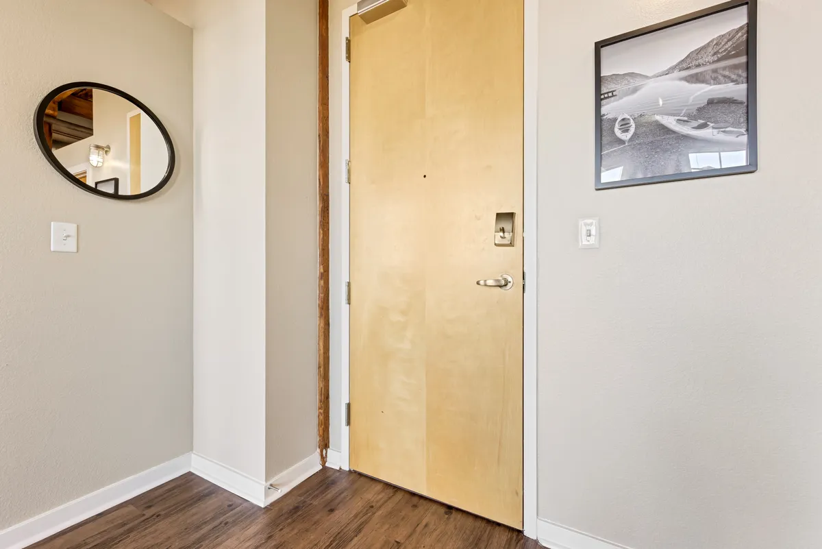 This image captures a welcoming entryway featuring a wooden door, a mirror, and a black and white photograph. The mood is inviting, setting the tone for first impressions as guests step inside. The space is uncluttered and thoughtfully decorated, suggesting a blend of classic elements and personal touches.