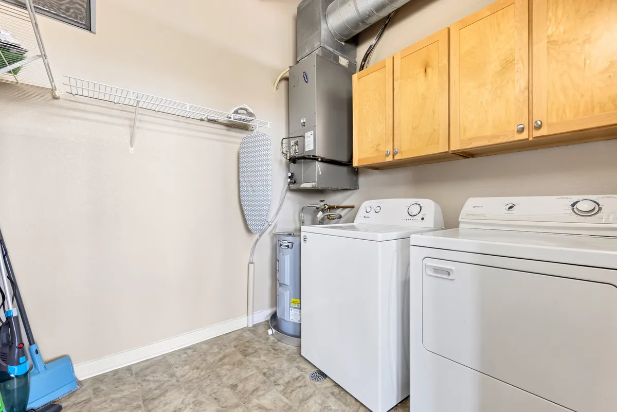 A well-organized laundry area featuring a washer, dryer, wooden cabinetry for storage, and an ironing board. The setting is bright and functional, emphasizing practical, in-home conveniences.